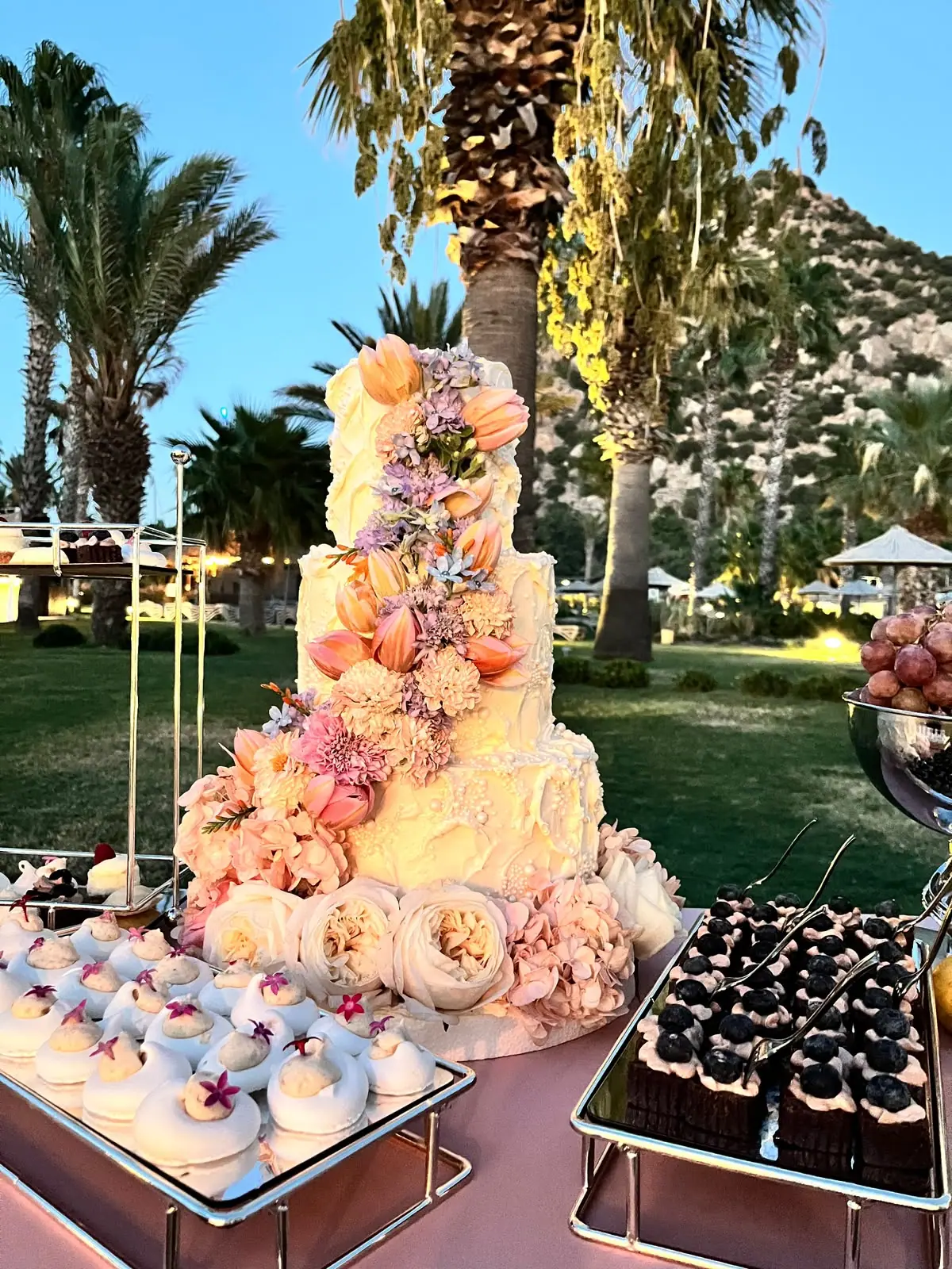 Tiered white wedding cake with flowers among palm trees